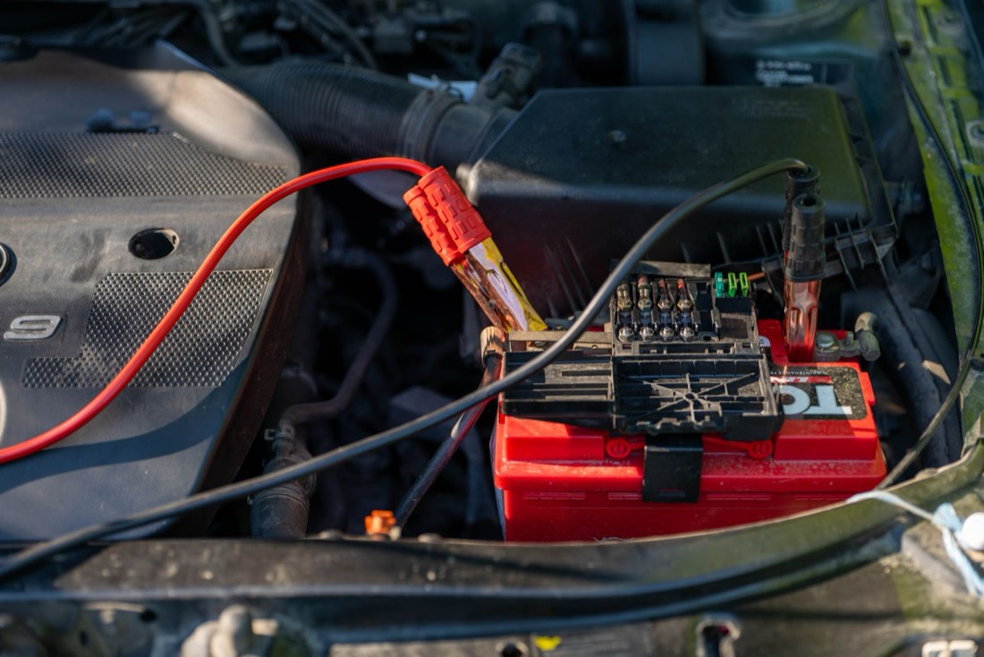 Pinces posées sur les bornes d’une batterie de voiture sous le capot