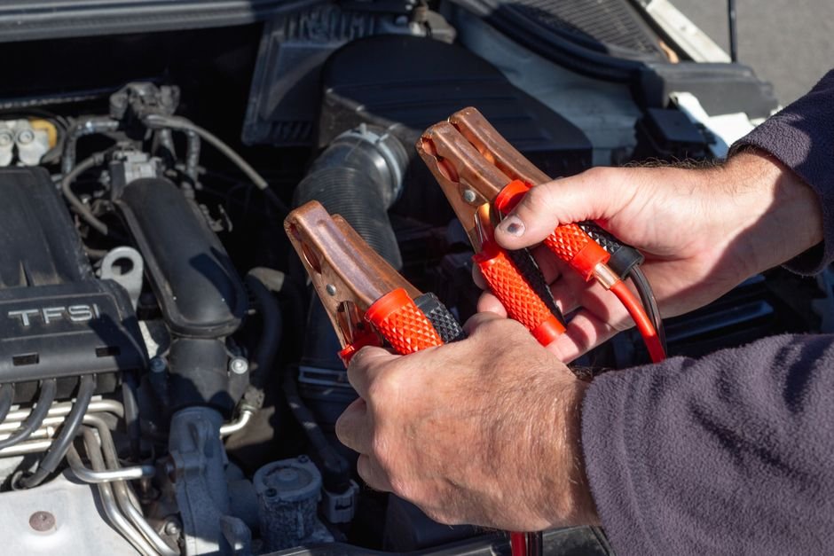 Mains tenant des pinces de démarrage près d'un moteur