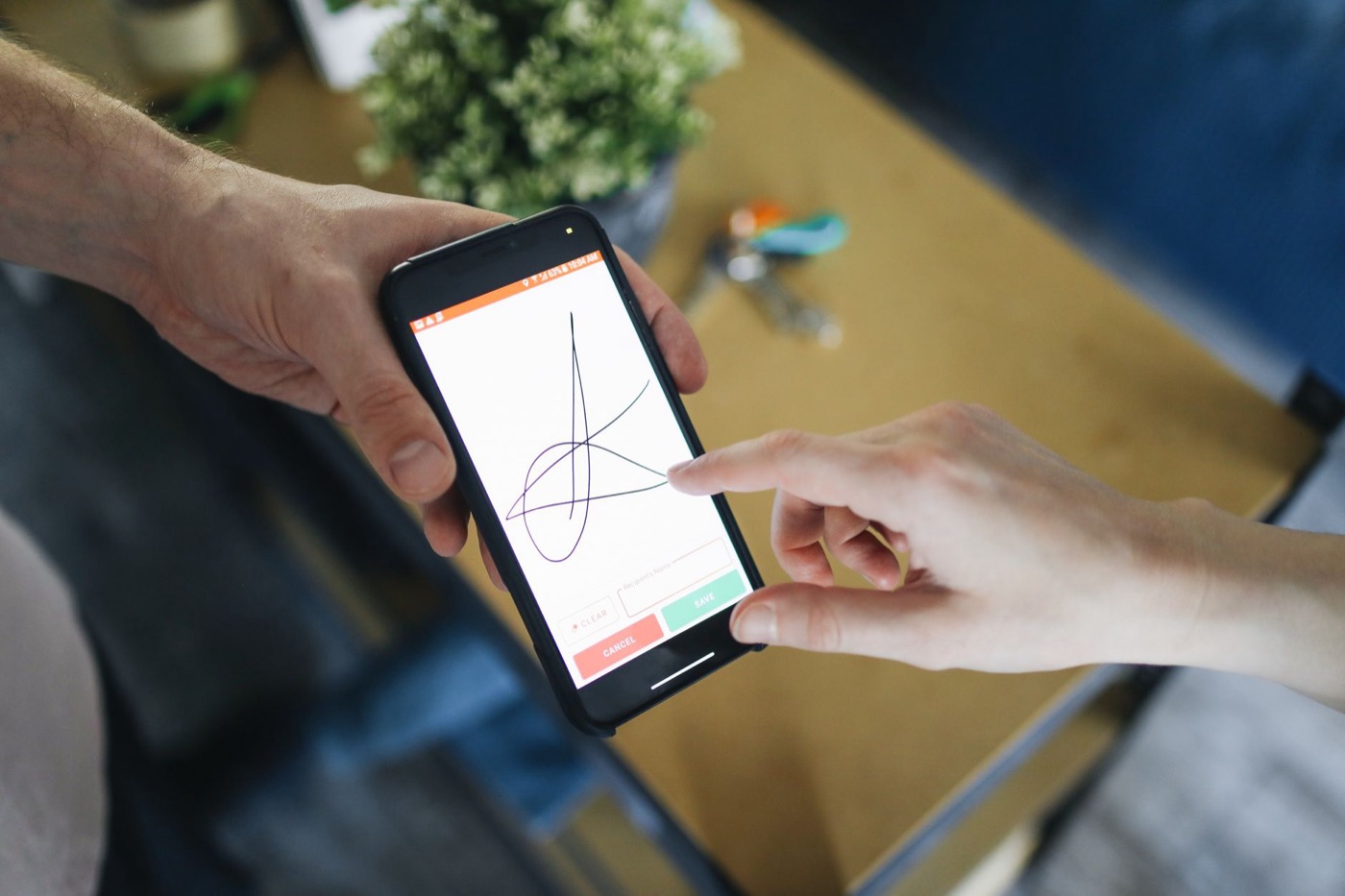 Signature au doigt sur l’écran d’un smartphone tenu par une autre personne