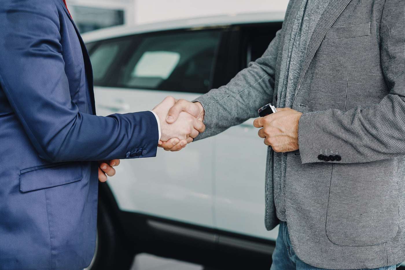 Poignée de main entre un vendeur et un client devant une voiture en concession