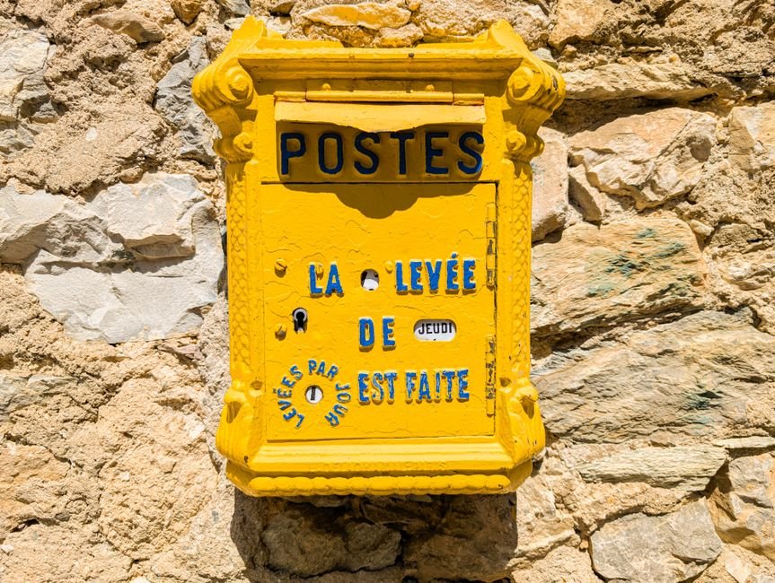 Boîte aux lettres jaune des Postes sur un mur de pierre