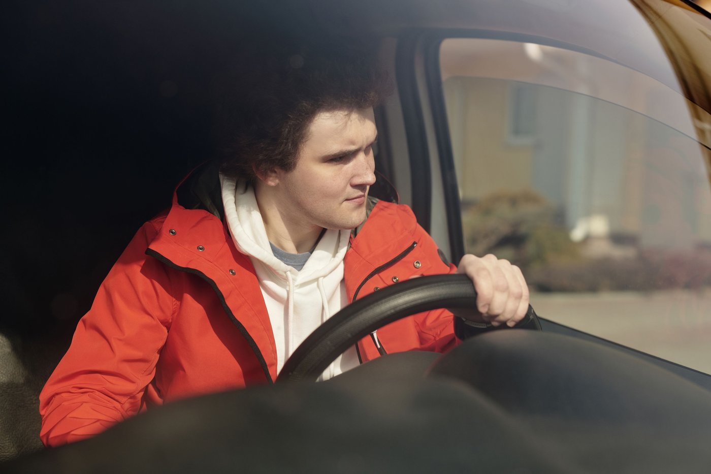 Jeune conducteur en veste rouge concentré au volant de sa voiture