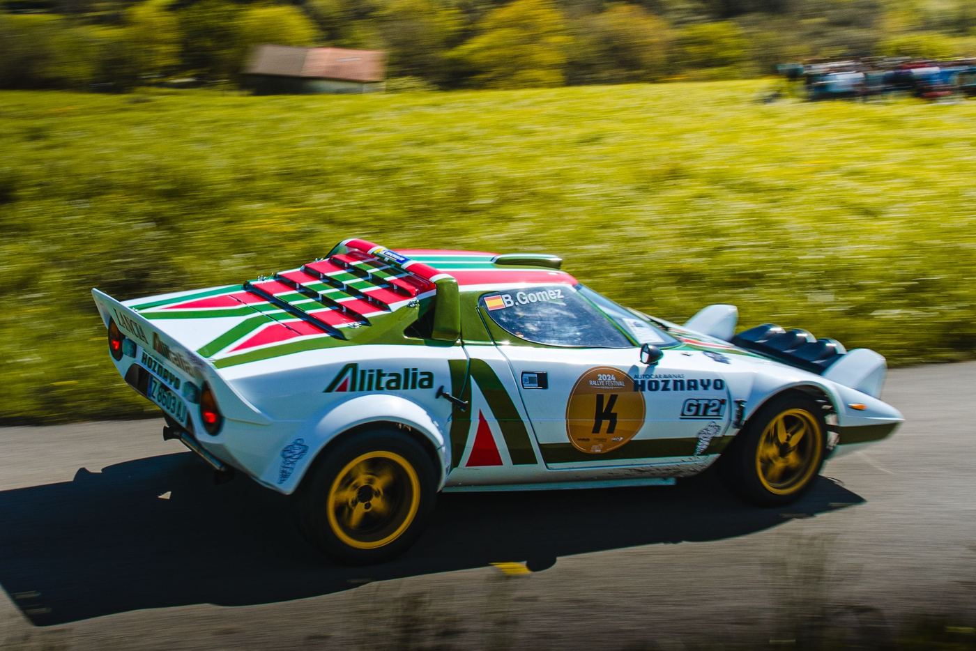 Lancia Stratos en livrée Alitalia vue de trois quarts arrière sur une route de rallye