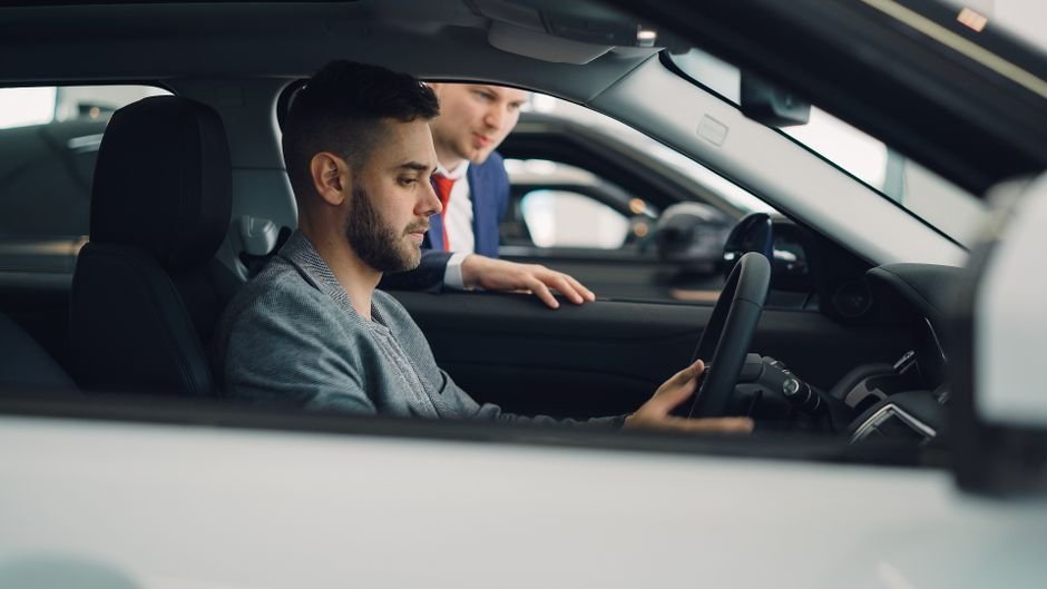 Conducteur installé au volant d'une voiture neuve avec un vendeur