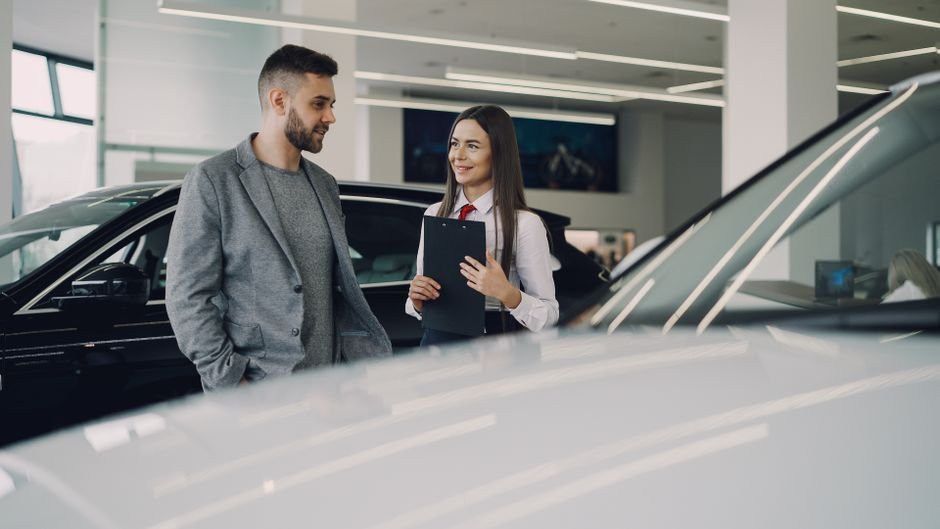 Client et vendeuse discutant devant des voitures neuves en concession