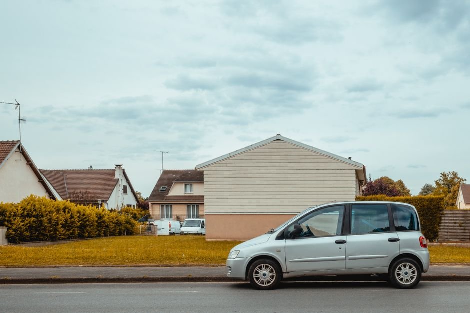 Vieille voiture thermique garée devant des pavillons de banlieue