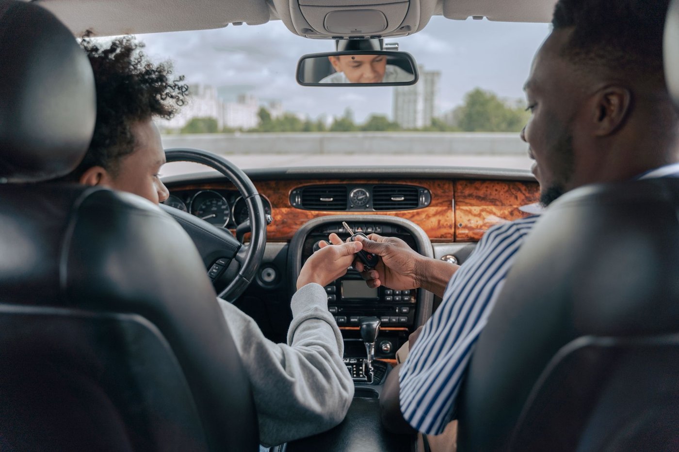 Adulte tendant une clé de voiture à un jeune installé au volant
