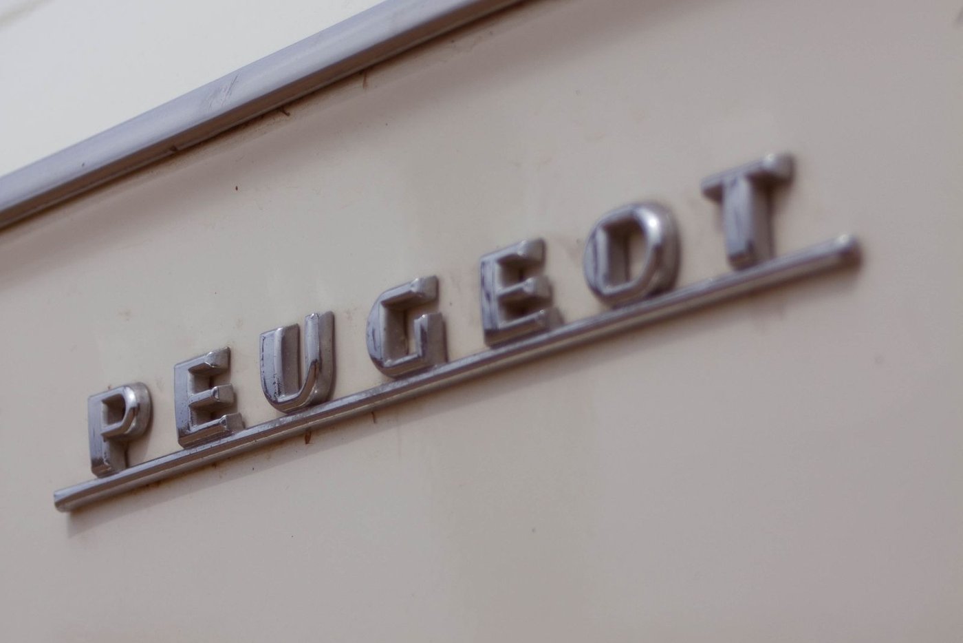 Monogramme Peugeot en lettres chromées sur une carrosserie claire