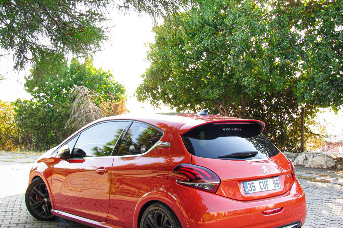 Peugeot 208 rouge de première génération garée sous les arbres