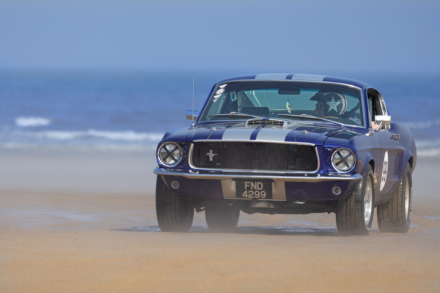 Shelby Mustang 1967 bleue à bandes blanches roulant sur une plage