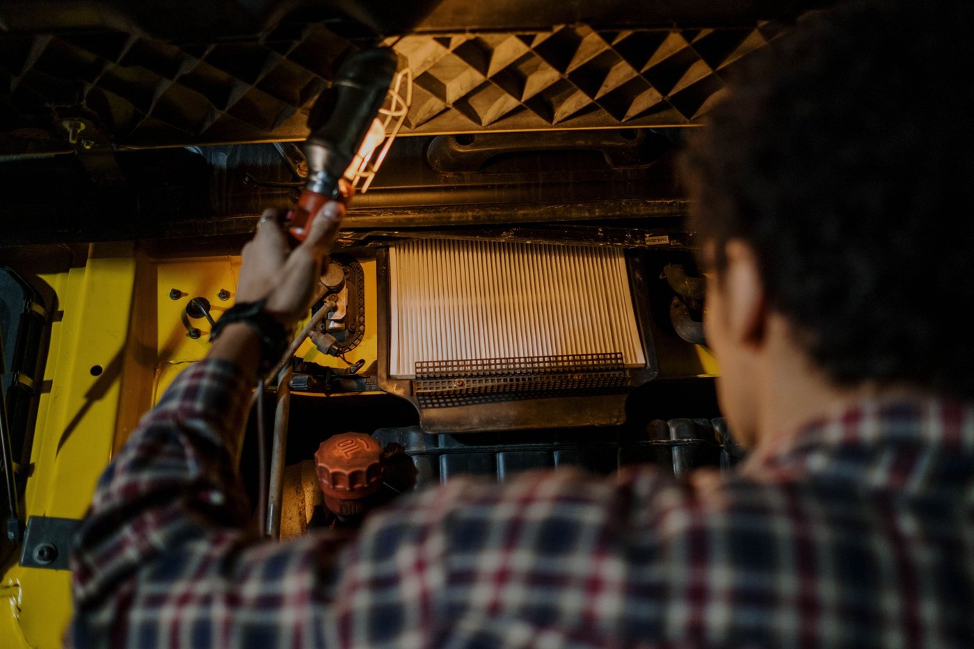Mécanicien éclairant un compartiment moteur, filtre à air plissé visible dans son boîtier